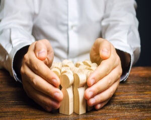 Man holding together a group of wooden people figurines in both hands on a table